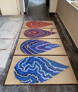 Image of four colorful works (again in the shape of teardrops) lying flat on the floor. Maybe on wood boards..